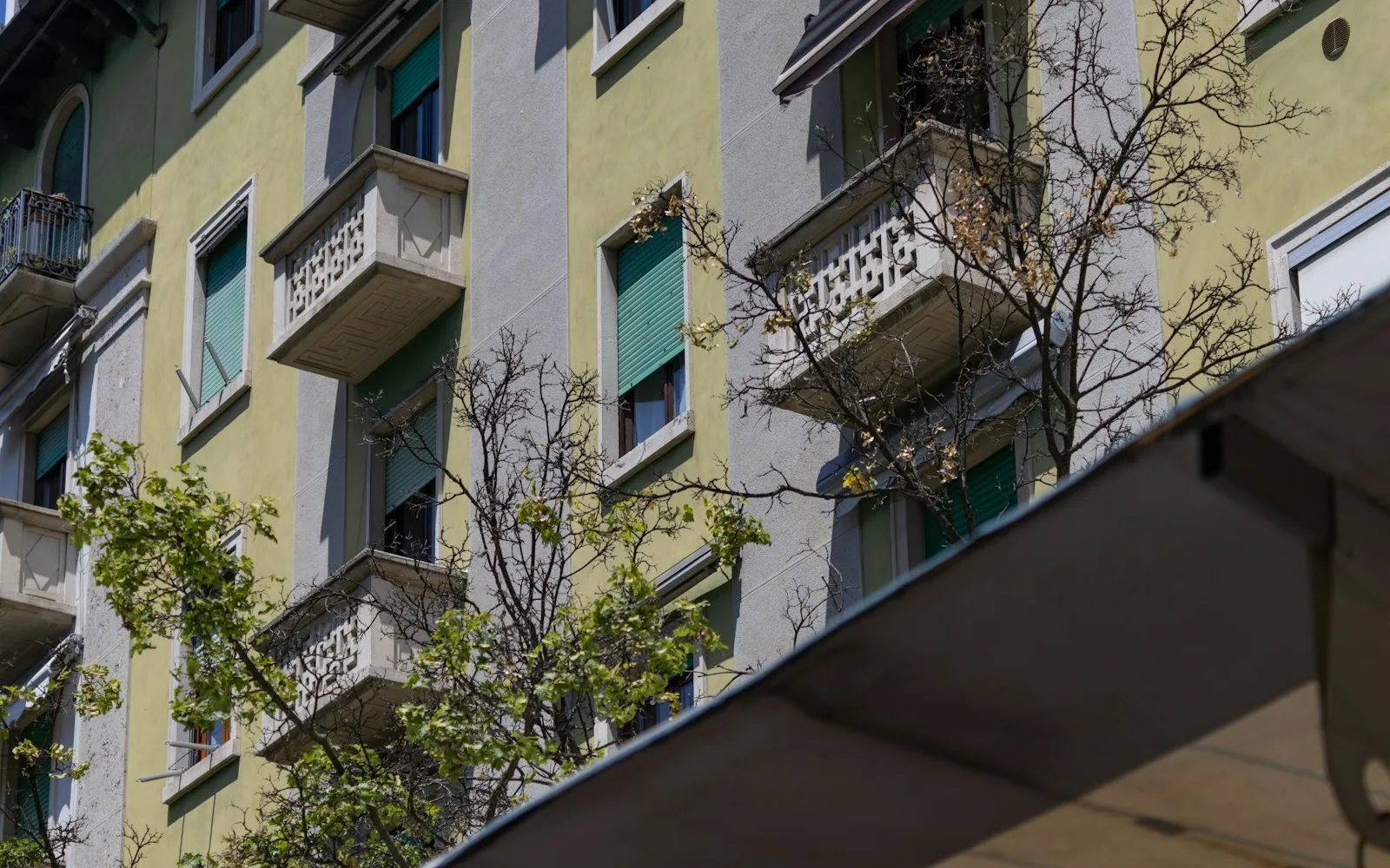 Facciata di un palazzo residenziale italiano con persiane verdi, balconcini in pietra e unità di condizionamento aggiunte.