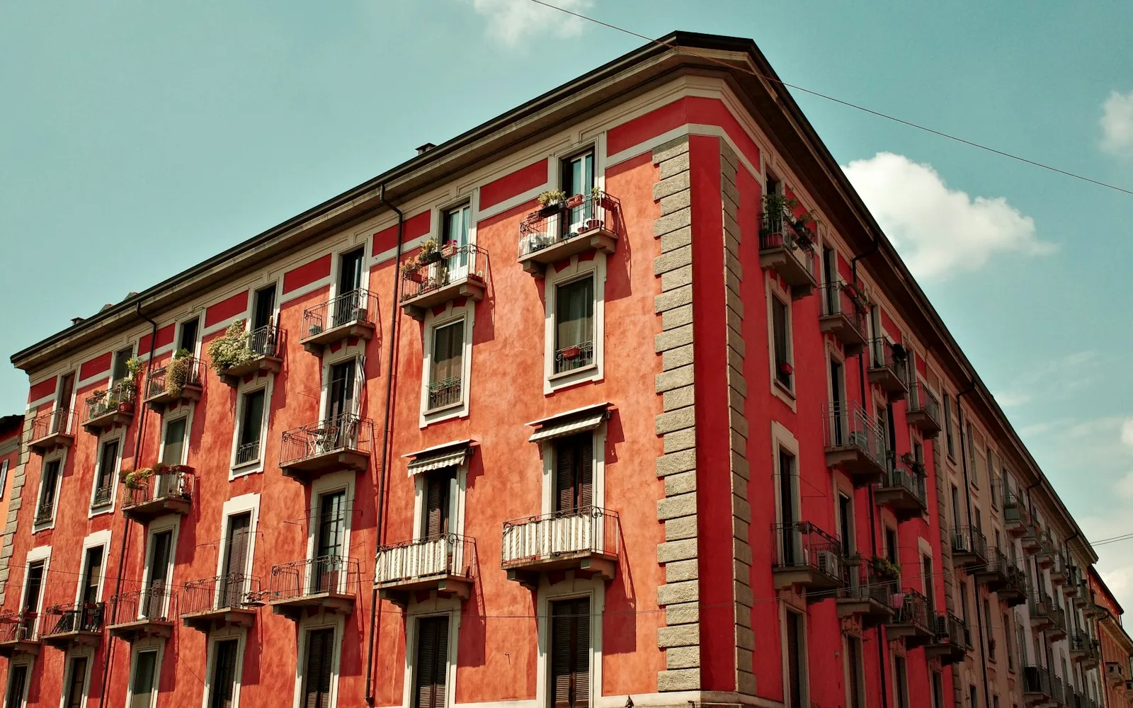 Angolo di un edificio residenziale rosso sui Navigli a Milano, con balconi e finestre ripetuti su più piani.