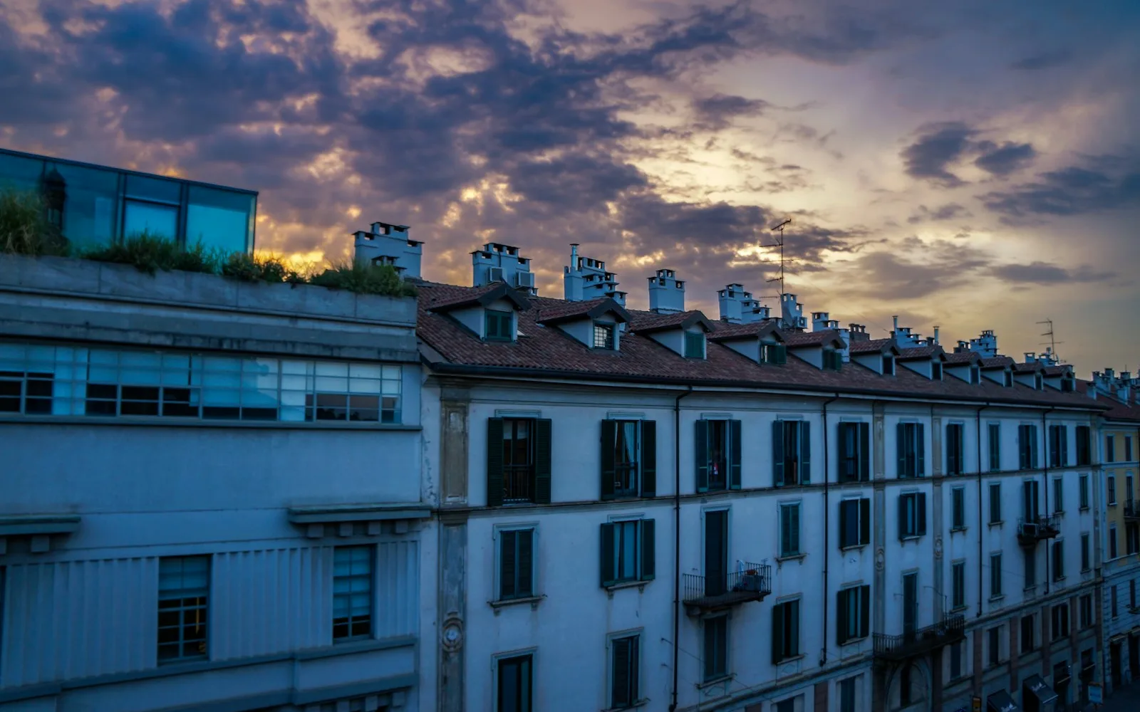 Tetti e facciate di palazzi milanesi al tramonto, con persiane e balconi degli appartamenti vicini.