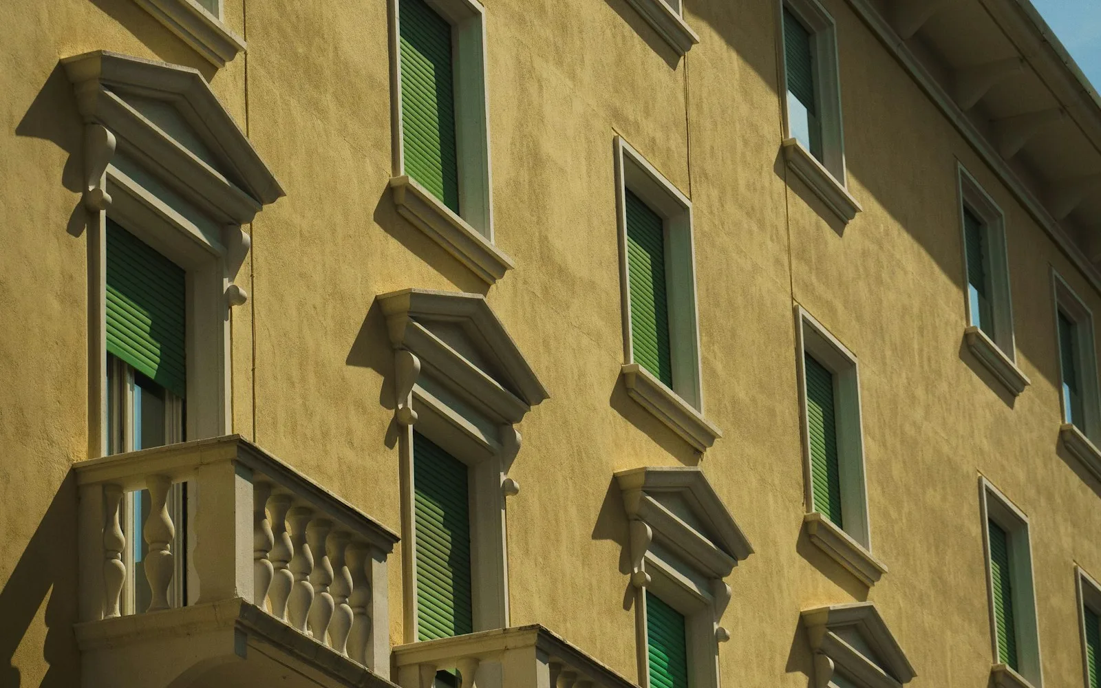 Facciata ocra di un palazzo milanese con persiane verdi e balconi in pietra vista dal basso.