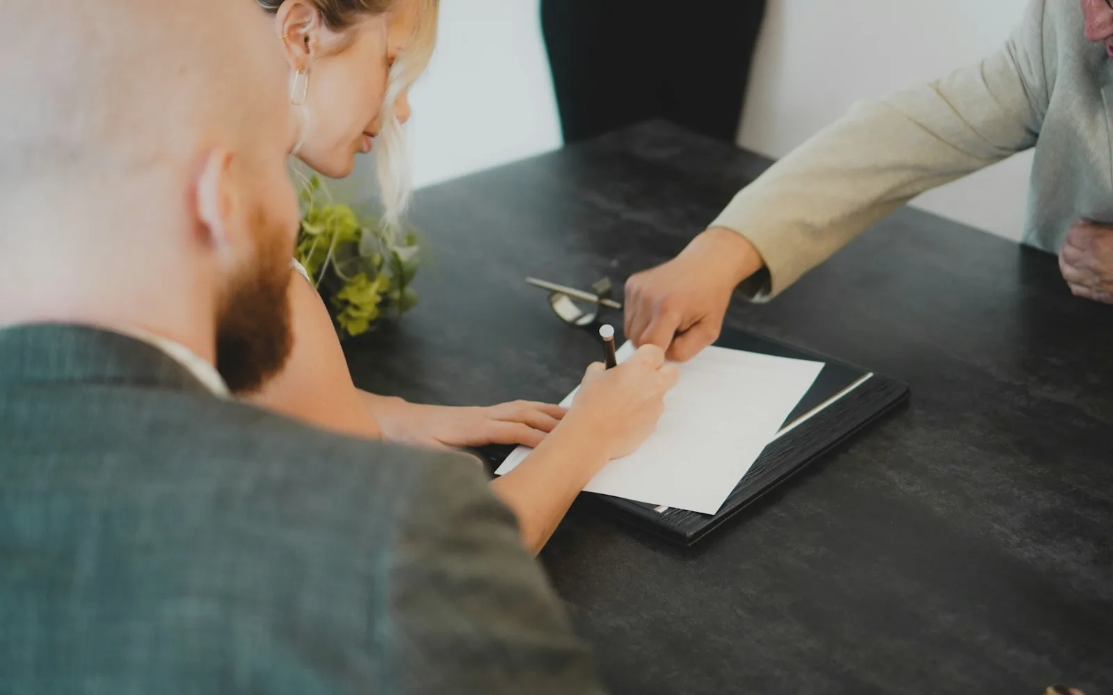 Persone sedute a un tavolo mentre firmano un documento con una penna.