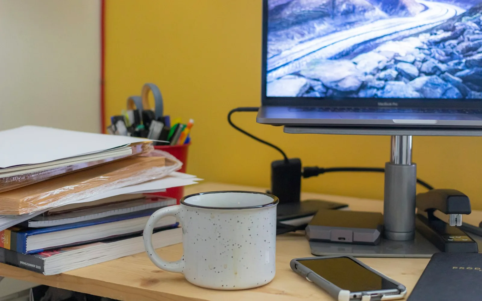 Scrivania con faldoni e documenti impilati accanto a una tazza.