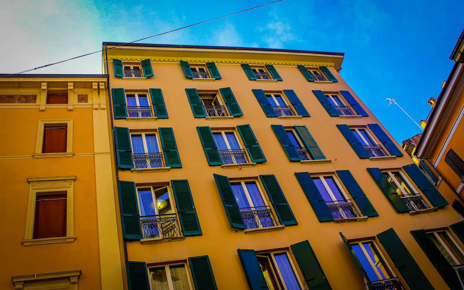 Palazzo italiano con facciata gialla appena tinteggiata, persiane verdi e balconcini in ferro.