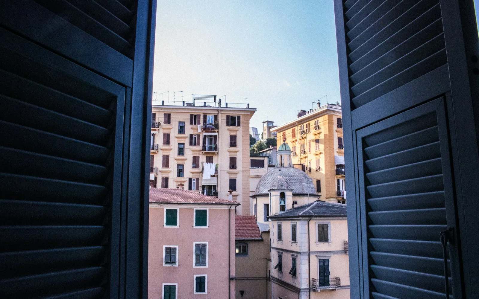 Persiane aperte su una vista di palazzi residenziali italiani dai colori pastello.