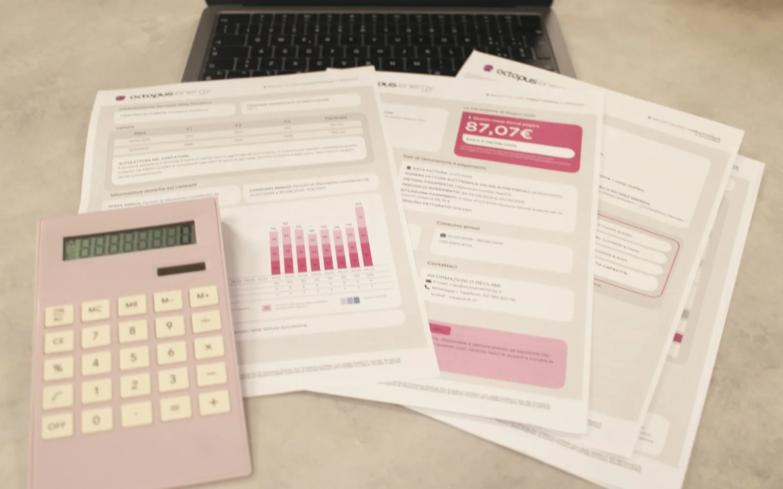 Bollette, una calcolatrice e un laptop su una scrivania per calcolare le spese di casa.