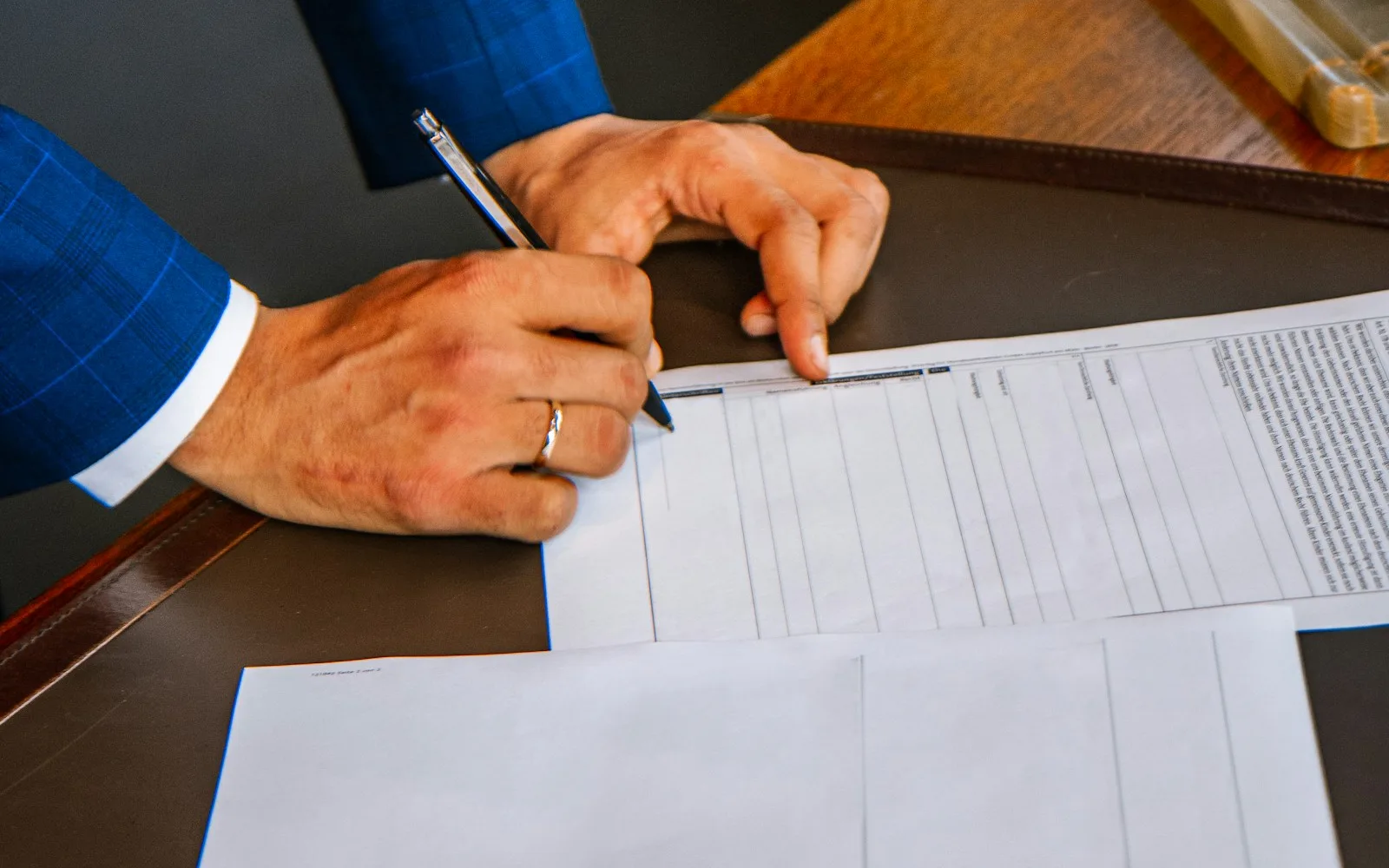 Persona che compila a mano un modulo a colonne su una scrivania in legno.