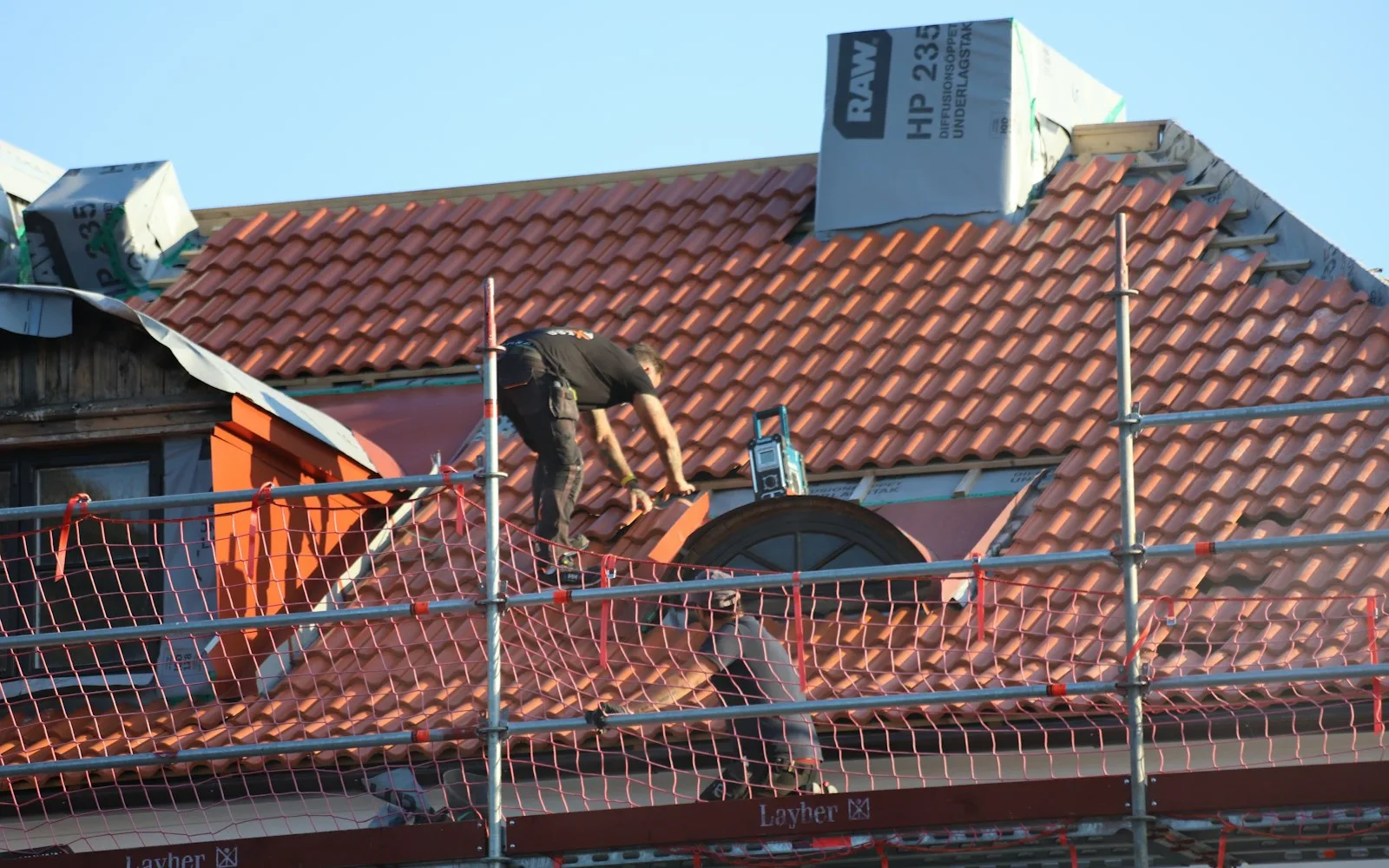 Operaio al lavoro sul tetto in tegole di un edificio residenziale con ponteggio.