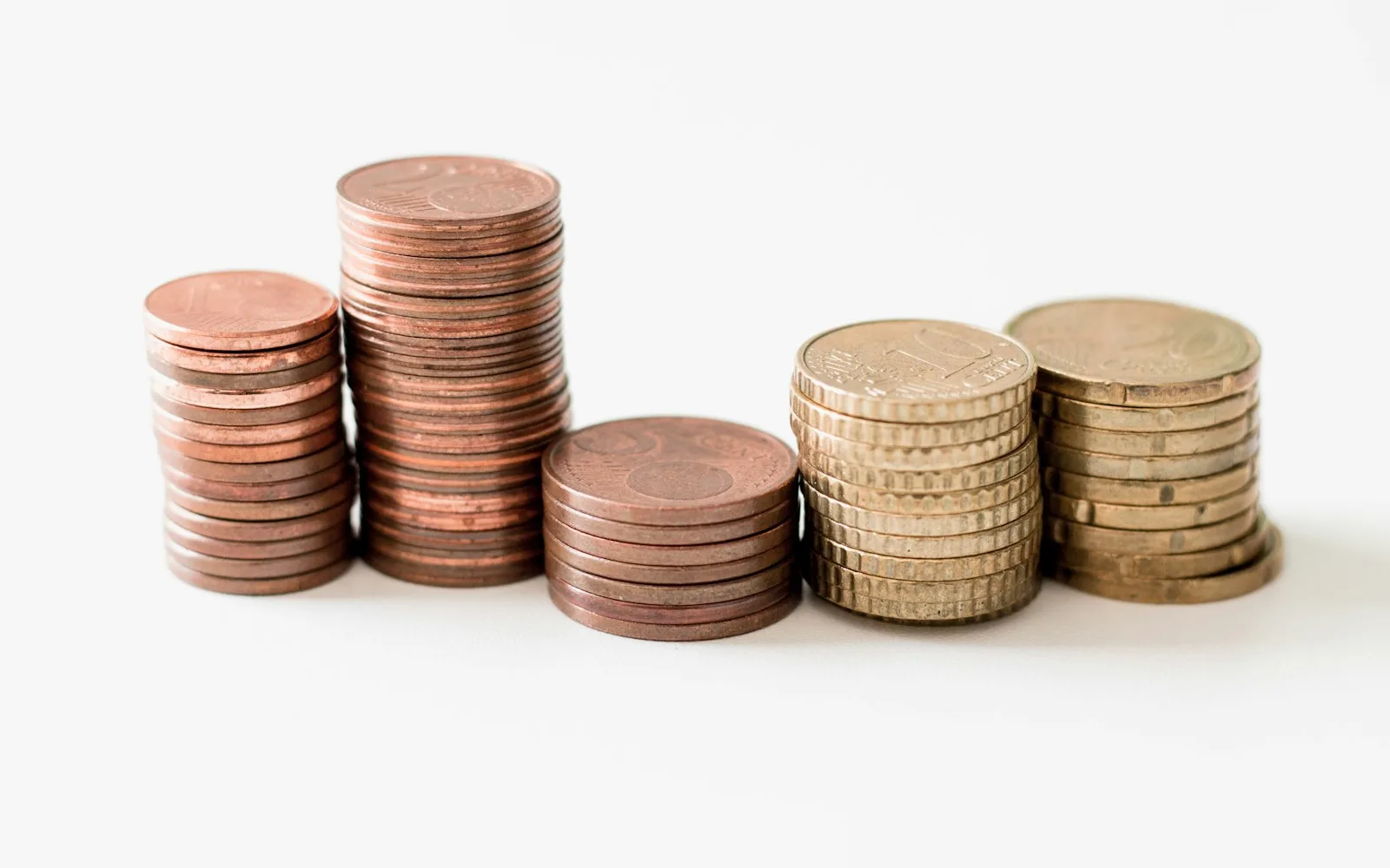 Pile di monete in euro di diversa altezza su sfondo bianco.