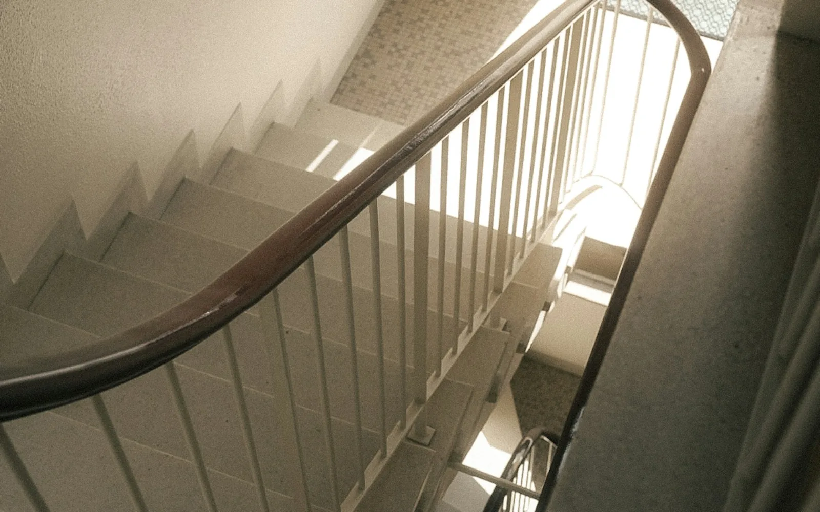 Vano scala di un palazzo con corrimano in legno, pianerottoli piastrellati e zerbino.