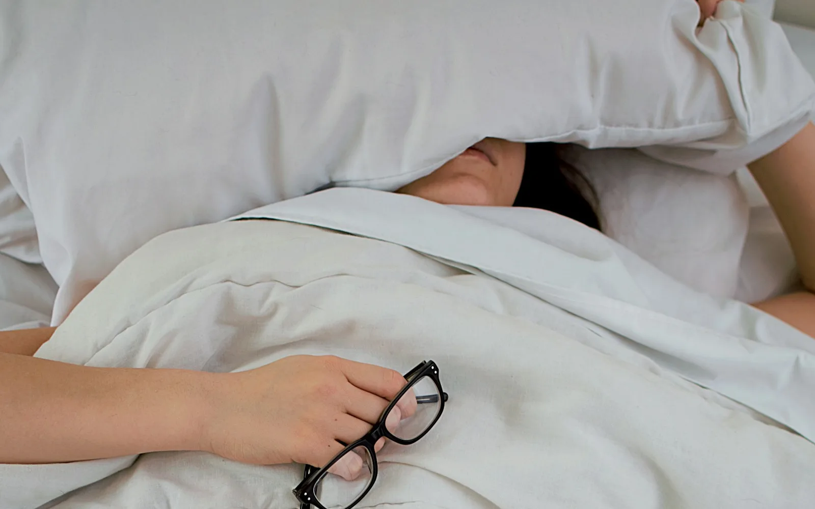 Persona a letto che si copre la testa con il cuscino per il rumore.